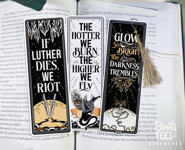 A set of three Penn Cole Kindred's Curse Bookmarks sit on an open book. The quotes read If Luther Dies We Riot, The Hotter We Burn the Higher we Fly, and Glow so Bright the darkness trembles